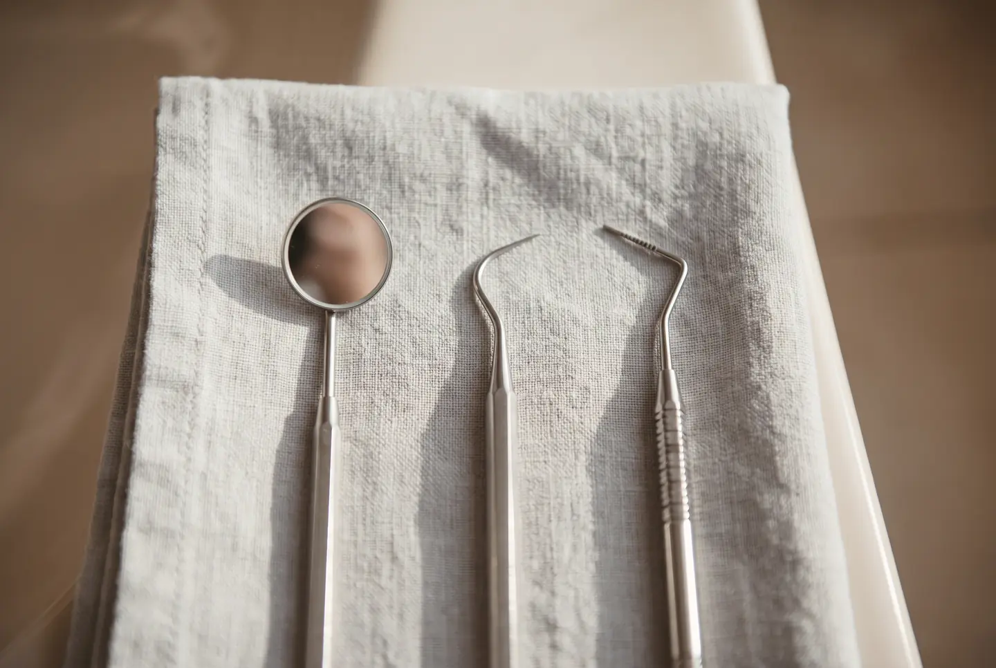 Polished stainless dental instruments arranged on folded pale grey linen